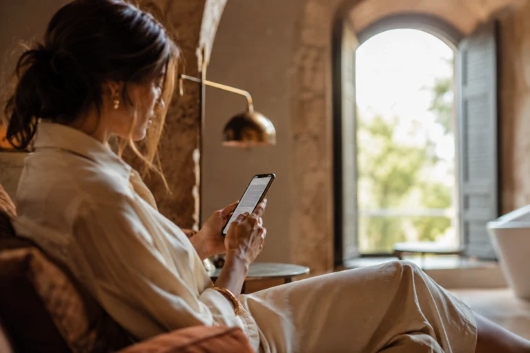 come aumentare le prenotazioni dirette — viaggiatrice consulta sito hotel boutique su smartphone, luce naturale mattutina